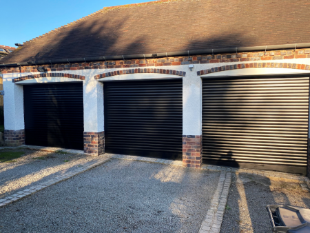 Trio of Black Roller Shutters installed on sloped ground.